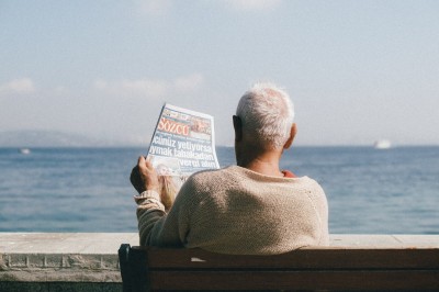 Senior číta noviny na lavičke pri mori